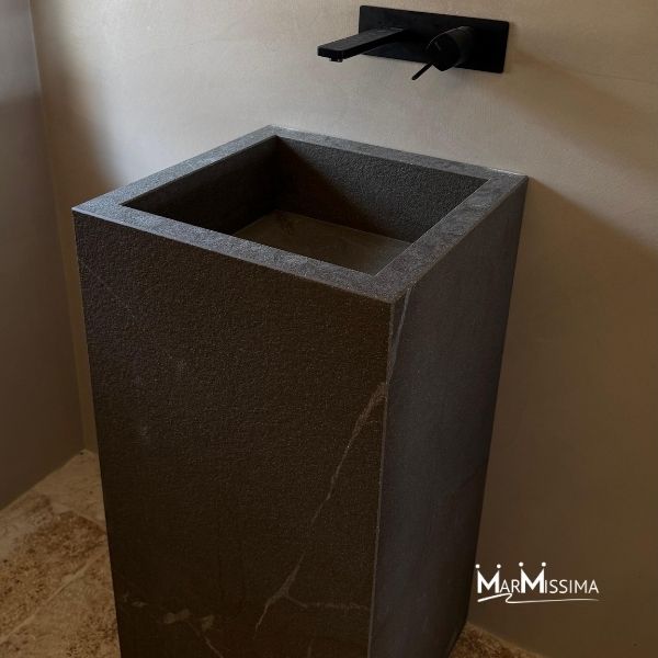 Lavabo da appoggio in pietra naturale nera, a forma di parallelepipedo con linee essenziali e superficie materica, installato con rubinetto a parete nero opaco in stile moderno