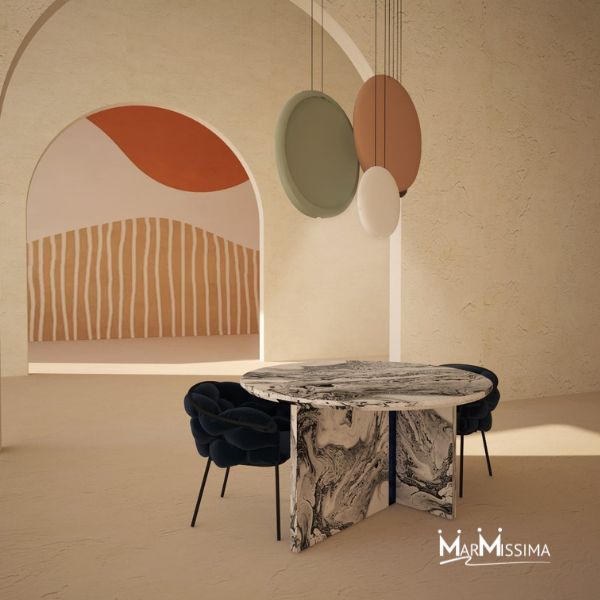 Tavolo rotondo di design in marmo con venature bianche e nere, base a pannelli incrociati, abbinato a sedie imbottite blu scuro in un ambiente moderno con archi e decorazioni artistiche a parete